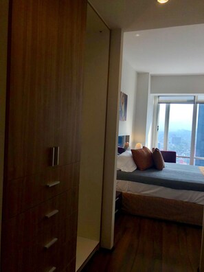 A bedroom with a large bed, a wooden wardrobe, and a city view through a large window. - Plaza Suites México City 2403 (Mexico City)