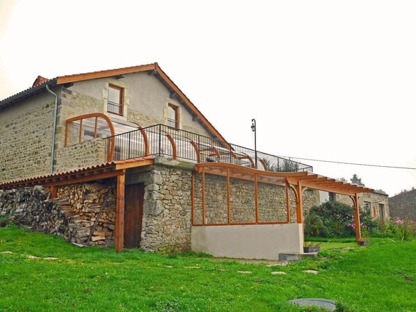 A stone house with a wooden balcony and a covered outdoor area. - Chambres d'hôtes du Plateau de la Danse (Saint-Etienne)