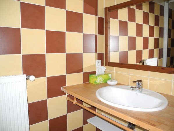 A bathroom with a checkered tile wall, a white sink, a wooden vanity, and a mirror. - Chambres d'hôtes du Plateau de la Danse (Saint-Etienne)