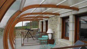 Un espace extérieur abrité, doté d’un mur en pierre, de poutres en bois et d’une table avec des chaises.