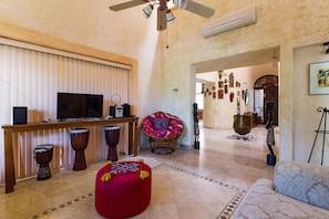 A living room with a television, drumming instruments, a red ottoman, a patterned sofa, and a ceiling fan.