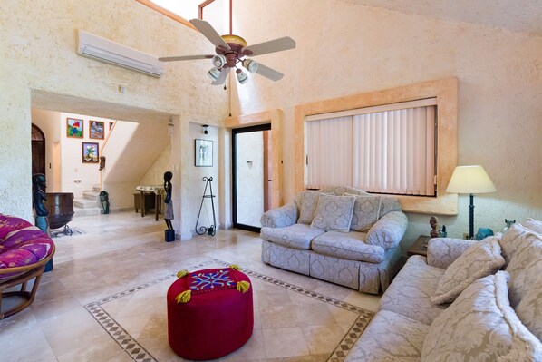 A spacious living room with a ceiling fan, a red ottoman, and patterned sofas. - Pakal by CocoBR (Playa del Carmen)