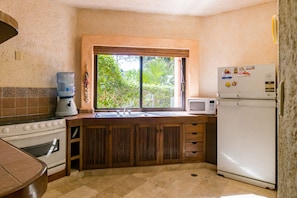 A compact kitchen with a sink, stove, and refrigerator, featuring a window with a view of greenery.