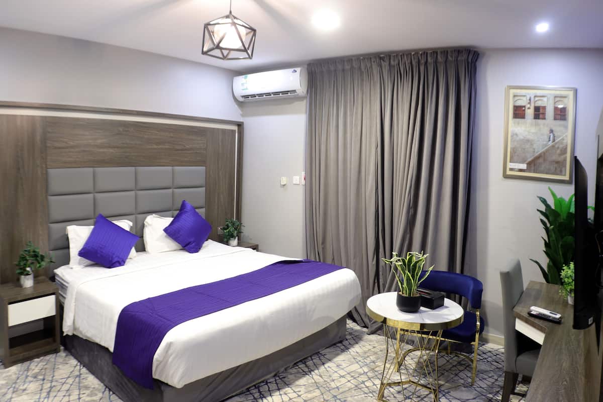 Habitación de hotel con una cama grande, una mesita redonda pequeña, una silla azul y una planta en maceta.