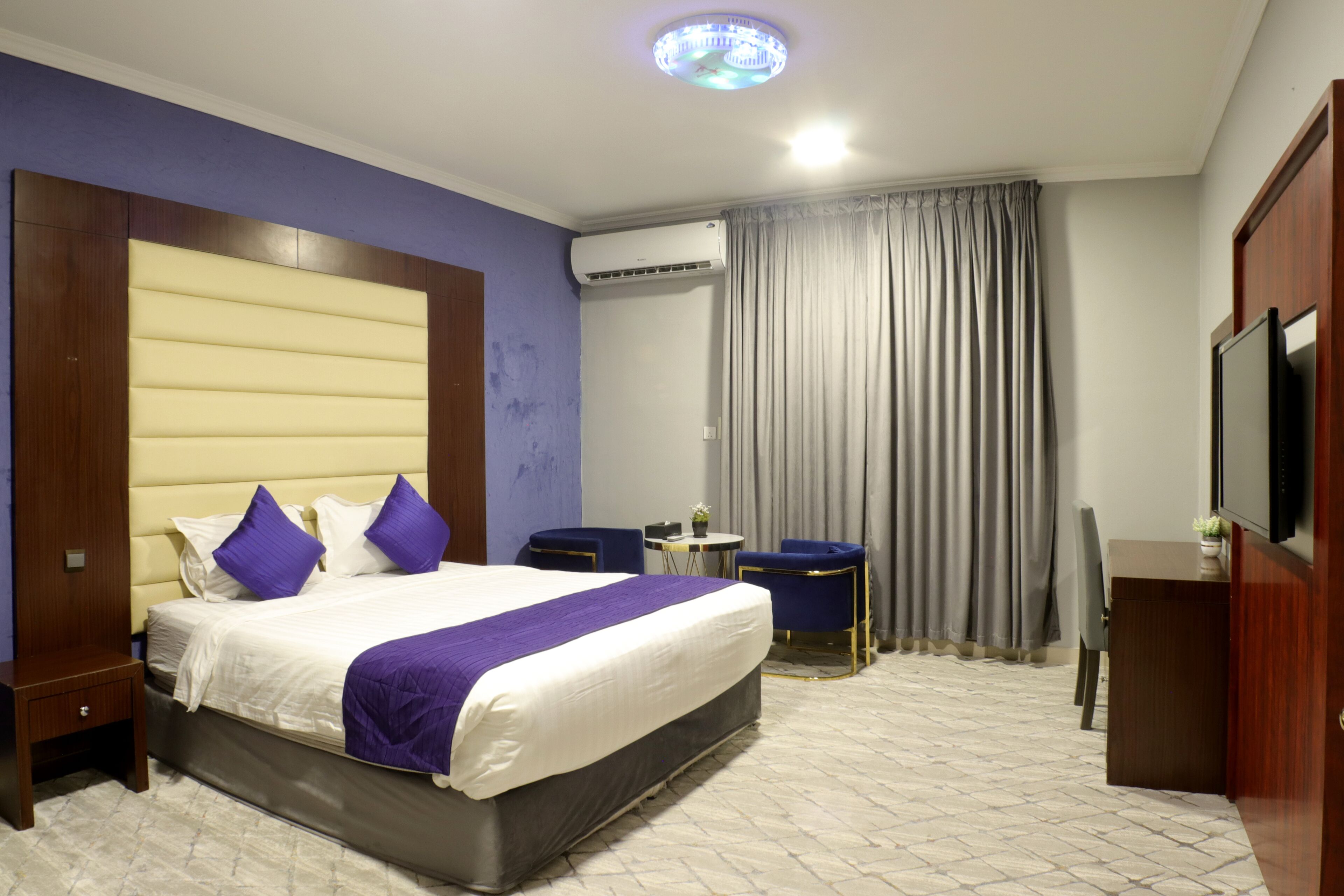 Habitación de hotel con una cama grande, un escritorio, una silla, un equipo de aire acondicionado y un televisor.