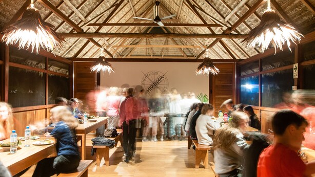 A restaurant with wooden tables and benches, a thatched roof, and a sign reading "Explorer Guides".