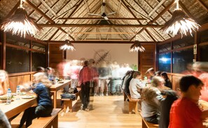 A restaurant with wooden tables and benches, a thatched roof, and a sign reading "Explorer Guides". -  Amazon Field Station byInkaterra (Las Piedras)