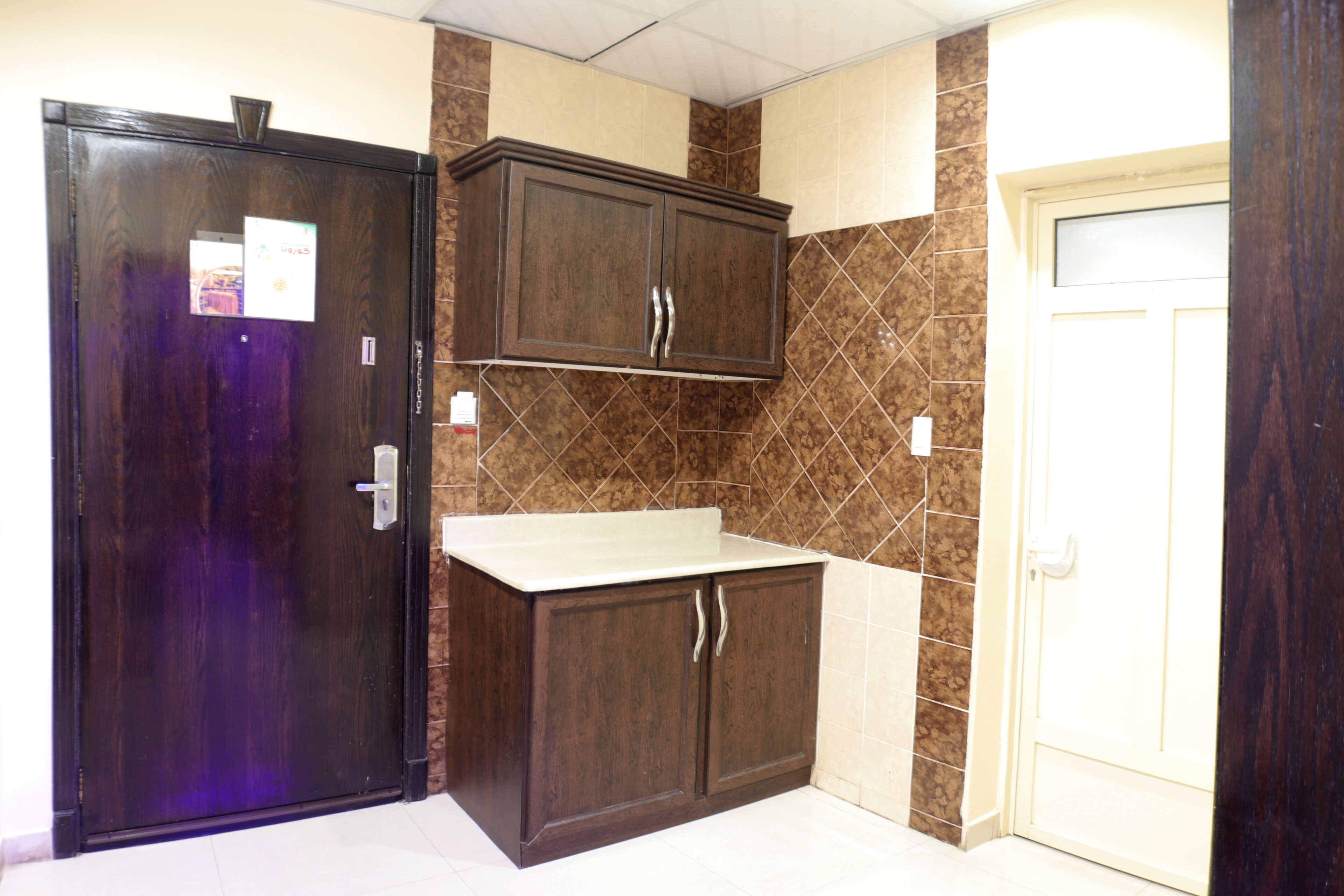 A room with a dark wooden door, a white countertop, and brown patterned walls.