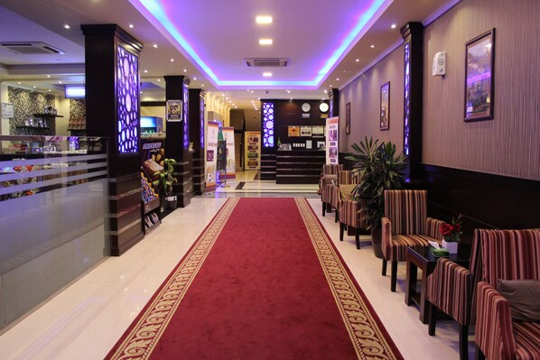 A hotel lobby with a red carpet, seating area, reception desk, and decorative wall panels.