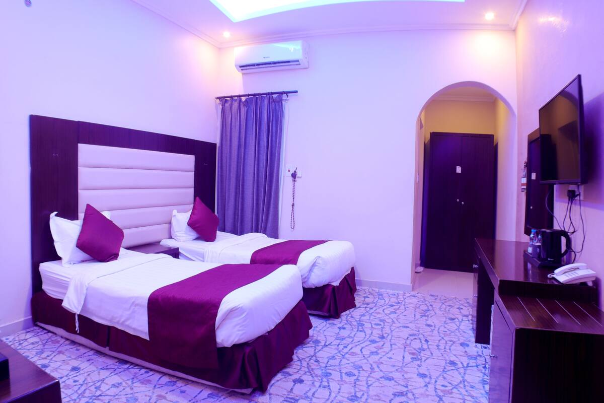 Habitación de hotel con dos camas, televisor, escritorio y aire acondicionado.