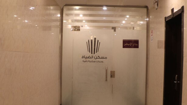A modern elevator with a logo and Arabic text, indicating a hotel entrance. - Maskan Al Dyafah Serviced Apartments 2 (Dammam)