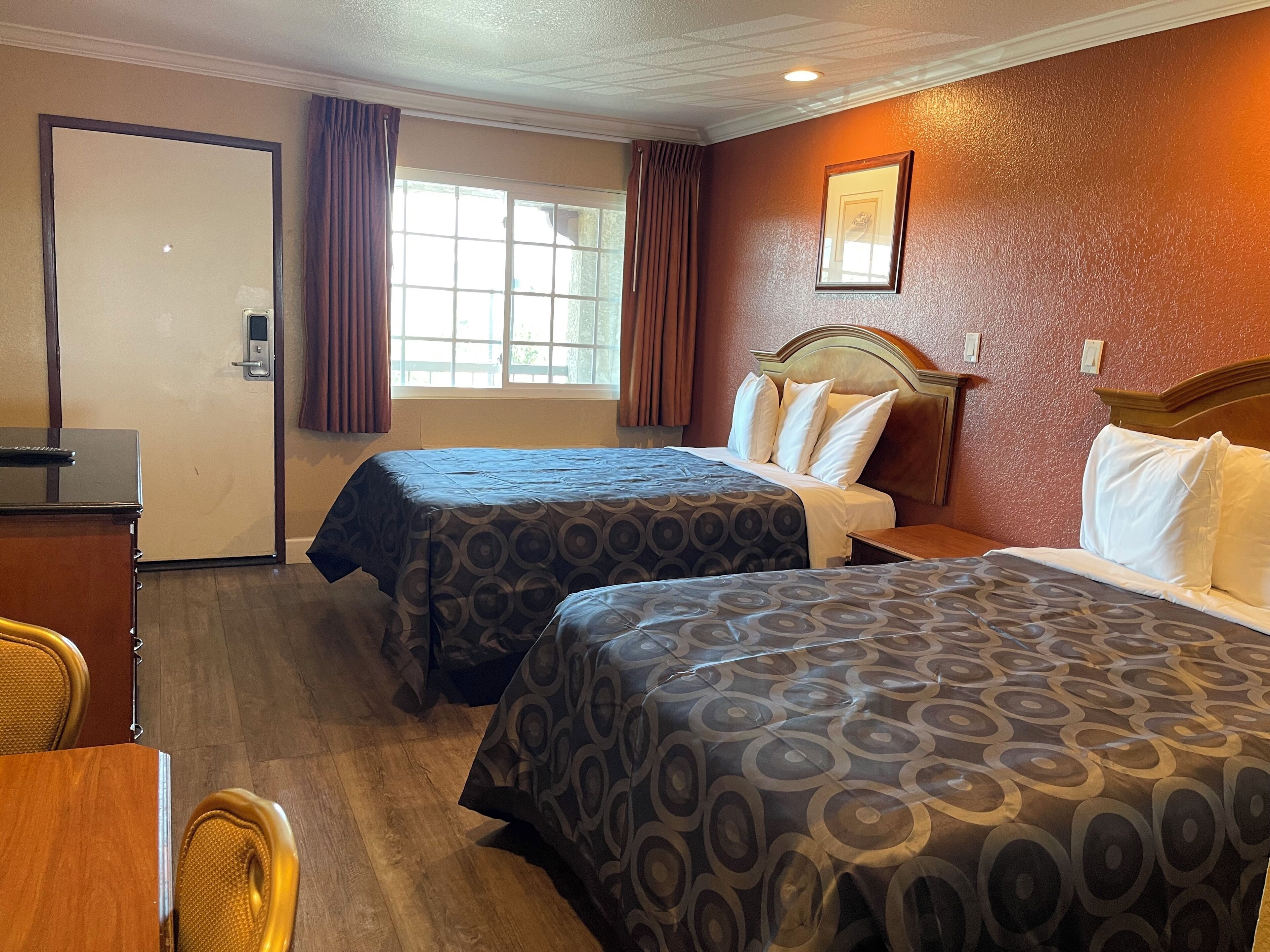 A hotel room with two beds, a desk, a chair, and a window with curtains.