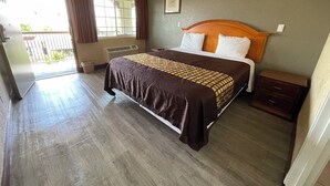 A hotel room with a large bed, a nightstand, a window with curtains, a radiator, and a door leading to a balcony. - Arlington Inn (Riverside)