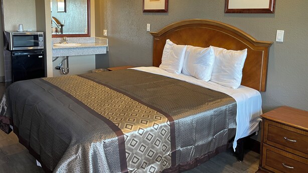 A hotel room with a bed, a wooden nightstand, a dresser, a microwave, and a sink with a mirror. - Arlington Inn (Riverside)