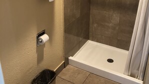 A shower area with a glass door, a toilet, and a towel rack with folded towels. - Arlington Inn (Riverside)