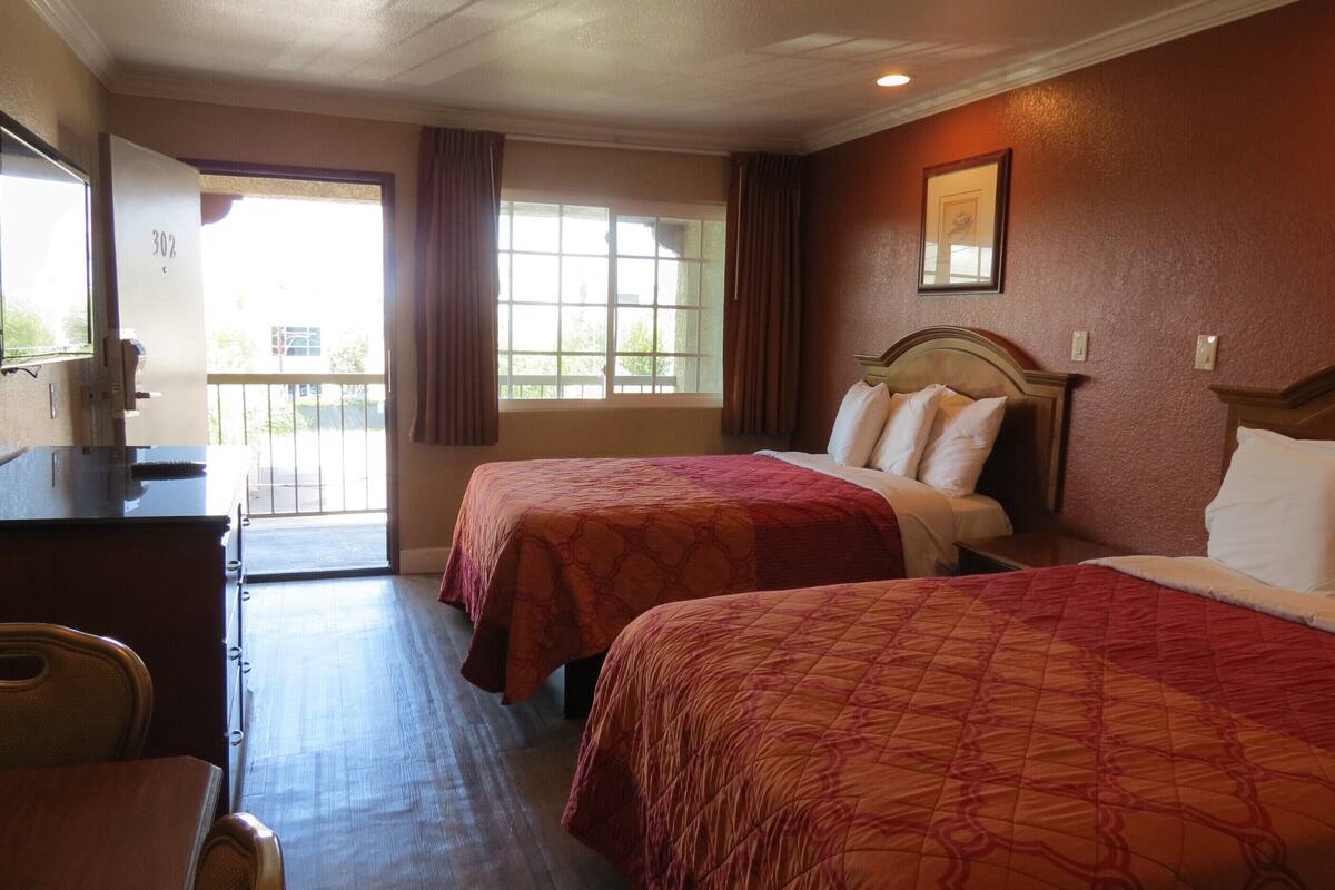 A hotel room with two beds, a desk, and a window with curtains.