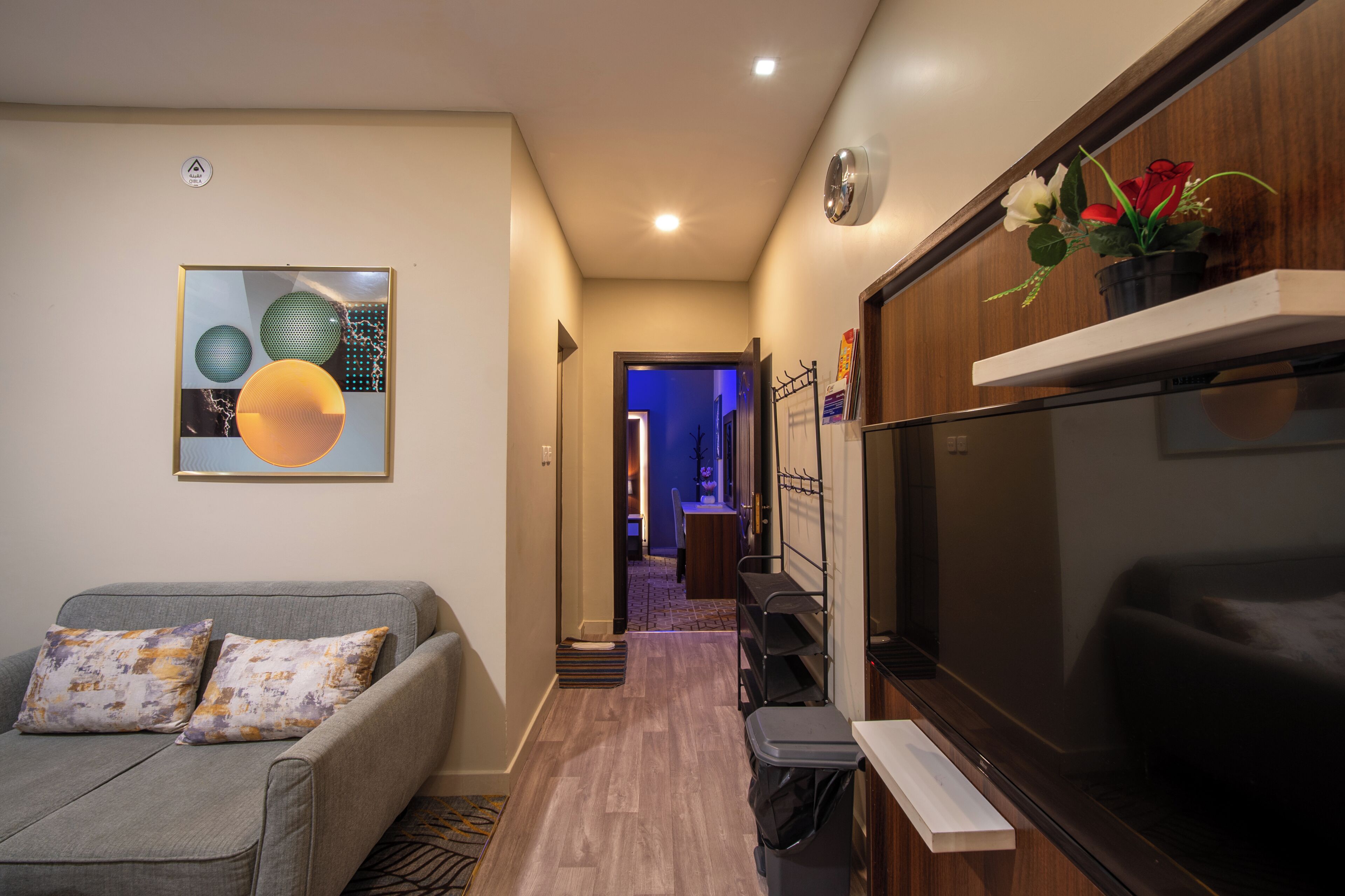 A modern living room with a grey sofa, a flat-screen TV, and a hallway leading to a dining area.