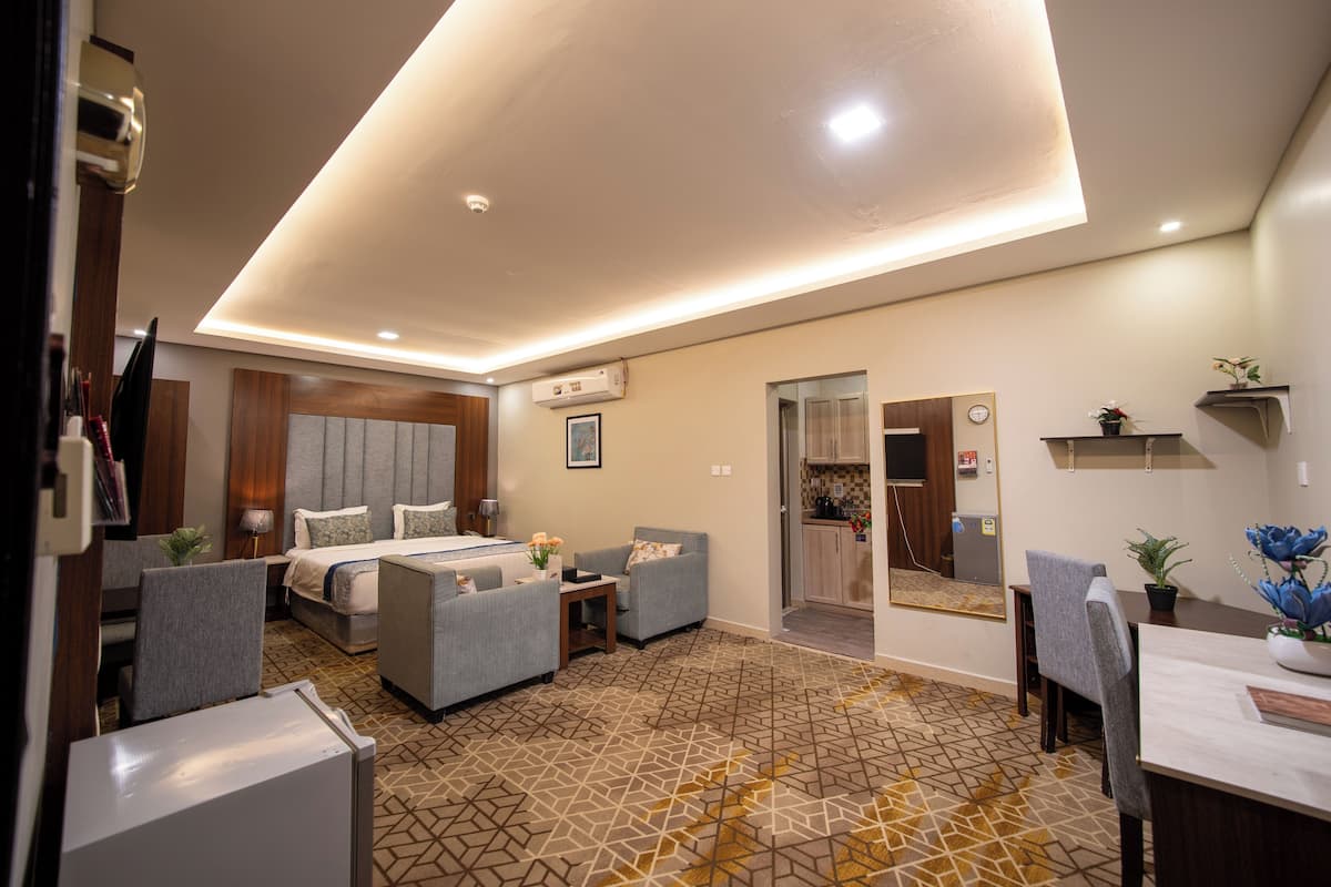 A modern hotel room with a bed, seating area, and a kitchenette.