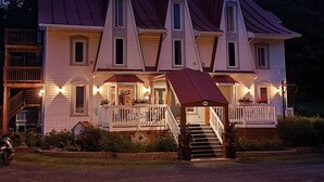 A large, multi-story house with a steeply pitched roof, multiple windows, and a front porch with railings. - Auberge Les Etchemins (Lac-Etchemin)