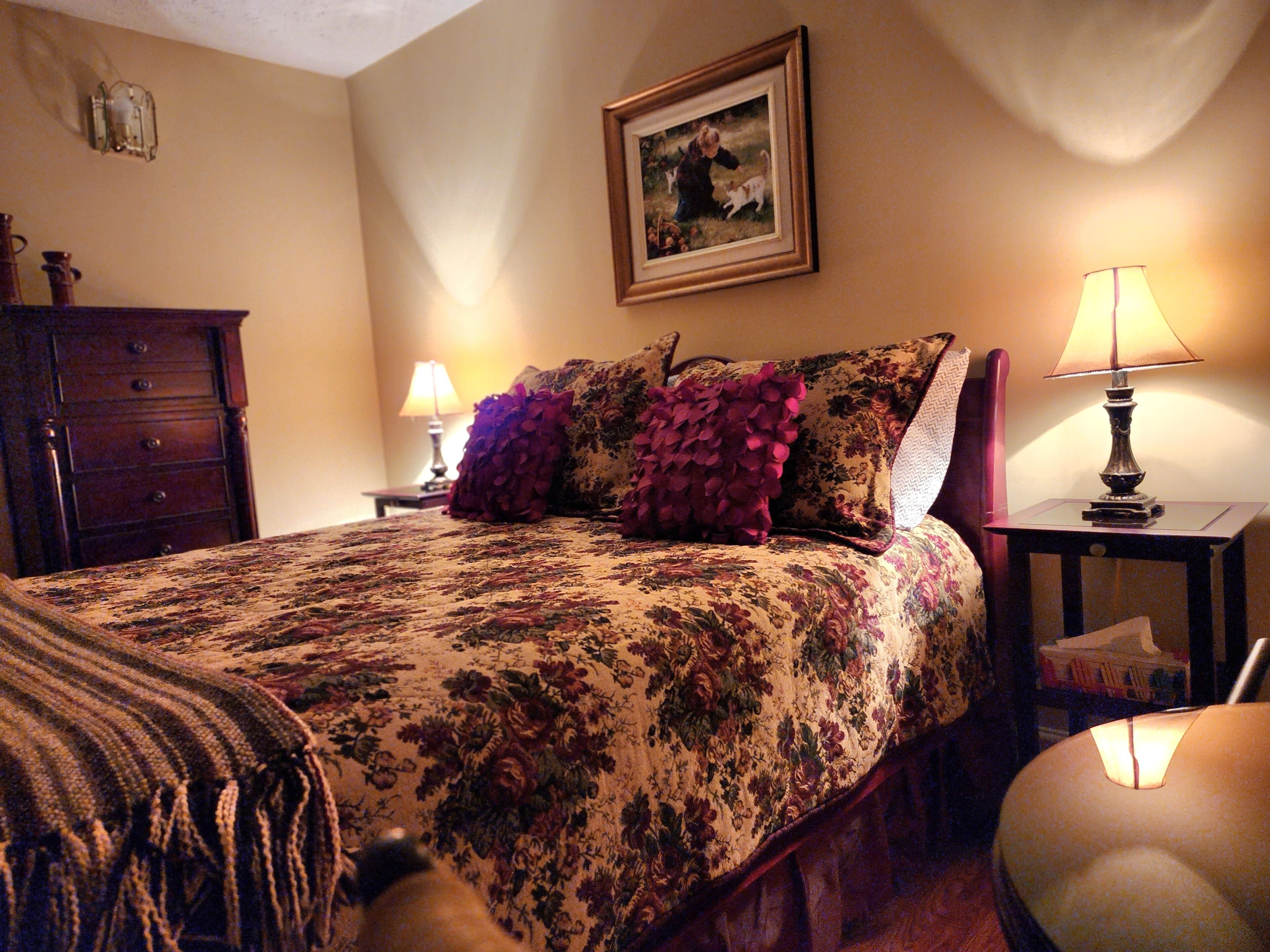 A neatly made bed with floral bedding, a framed picture on the wall, and two bedside lamps.