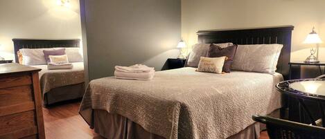 Una habitación de hotel con una cama grande, dos mesitas de noche, una silla y un aparador de madera.