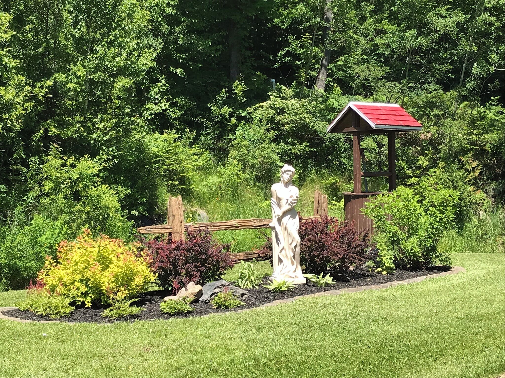 Un jardin agrémenté d’une statue, d’une clôture en bois et d’une construction au toit rouge.