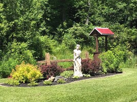 Un jardín con una estatua, una cerca de madera y una estructura con techo rojo.