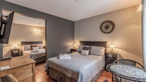 A hotel room with two beds, a desk, a chair, a TV, and a round table. - Auberge Les Etchemins (Lac-Etchemin)