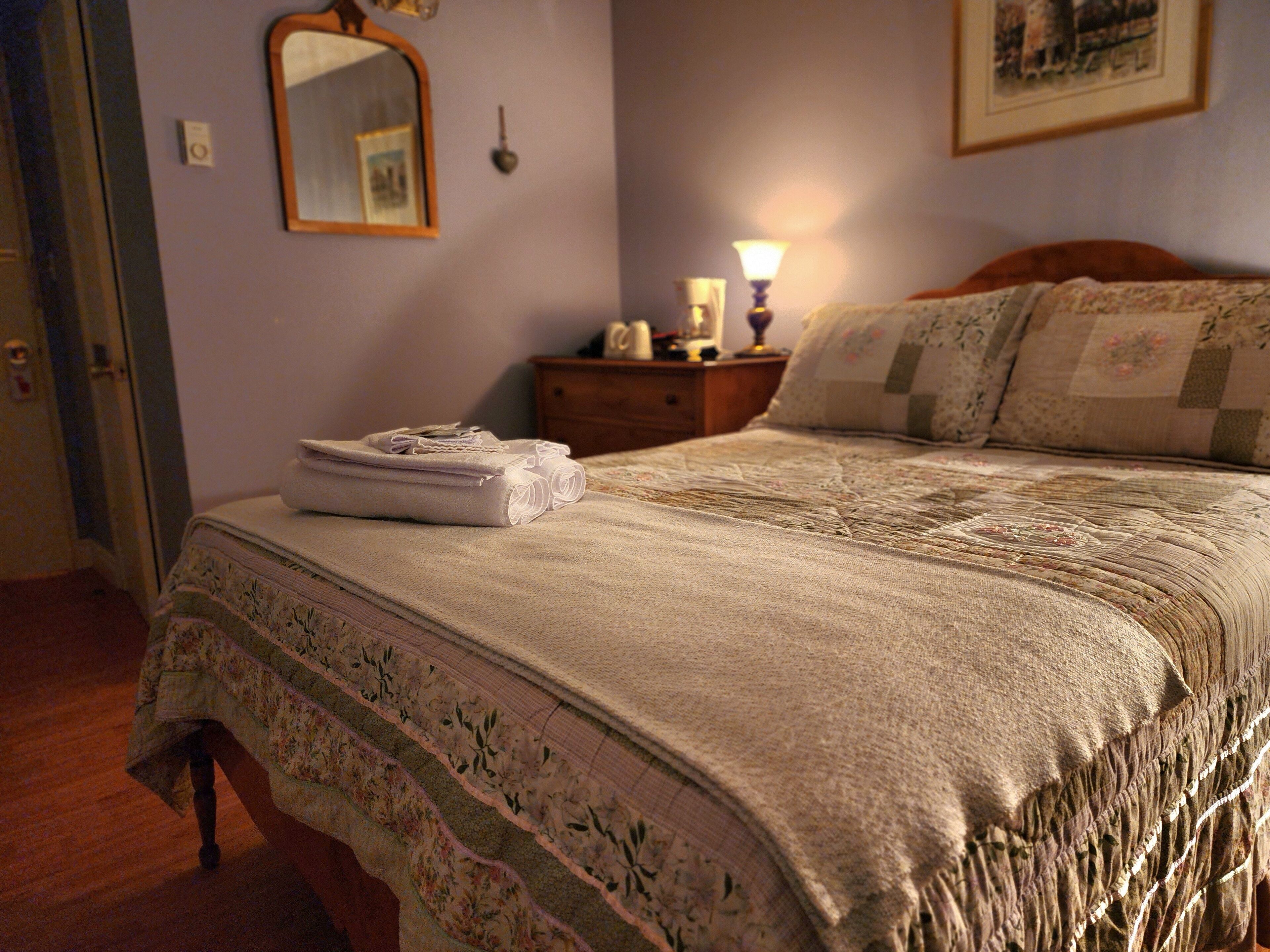 Un lit bien fait, avec une couvre-lit à motifs floraux et des oreillers, une lampe de chevet et une serviette pliée posée sur la table de chevet.