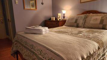 Una cama bien hecha con una colcha y almohadas estampadas con motivos florales, una lámpara de noche y una toalla doblada en la mesita.