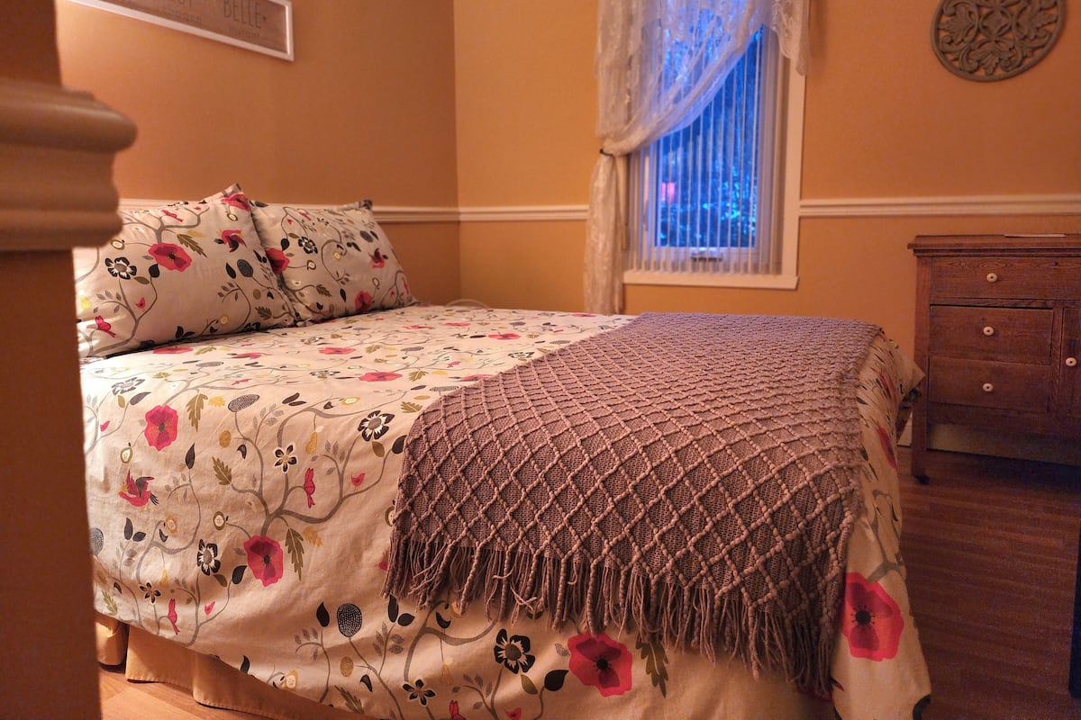 Une chambre à coucher avec une couvre-lit à motifs floraux, un plaid en tissu tissé et une table de chevet en bois.