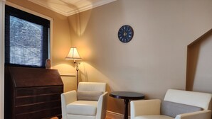 A room with two white armchairs, a small round table, a dark wooden cabinet, and a wall clock. - Auberge Les Etchemins (Lac-Etchemin)