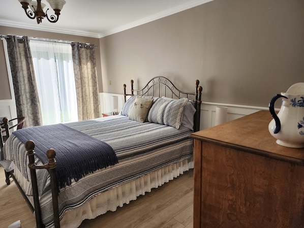 Un dormitorio con cama, mesita de noche, cómoda de madera, candelabro y ventana con cortinas.
