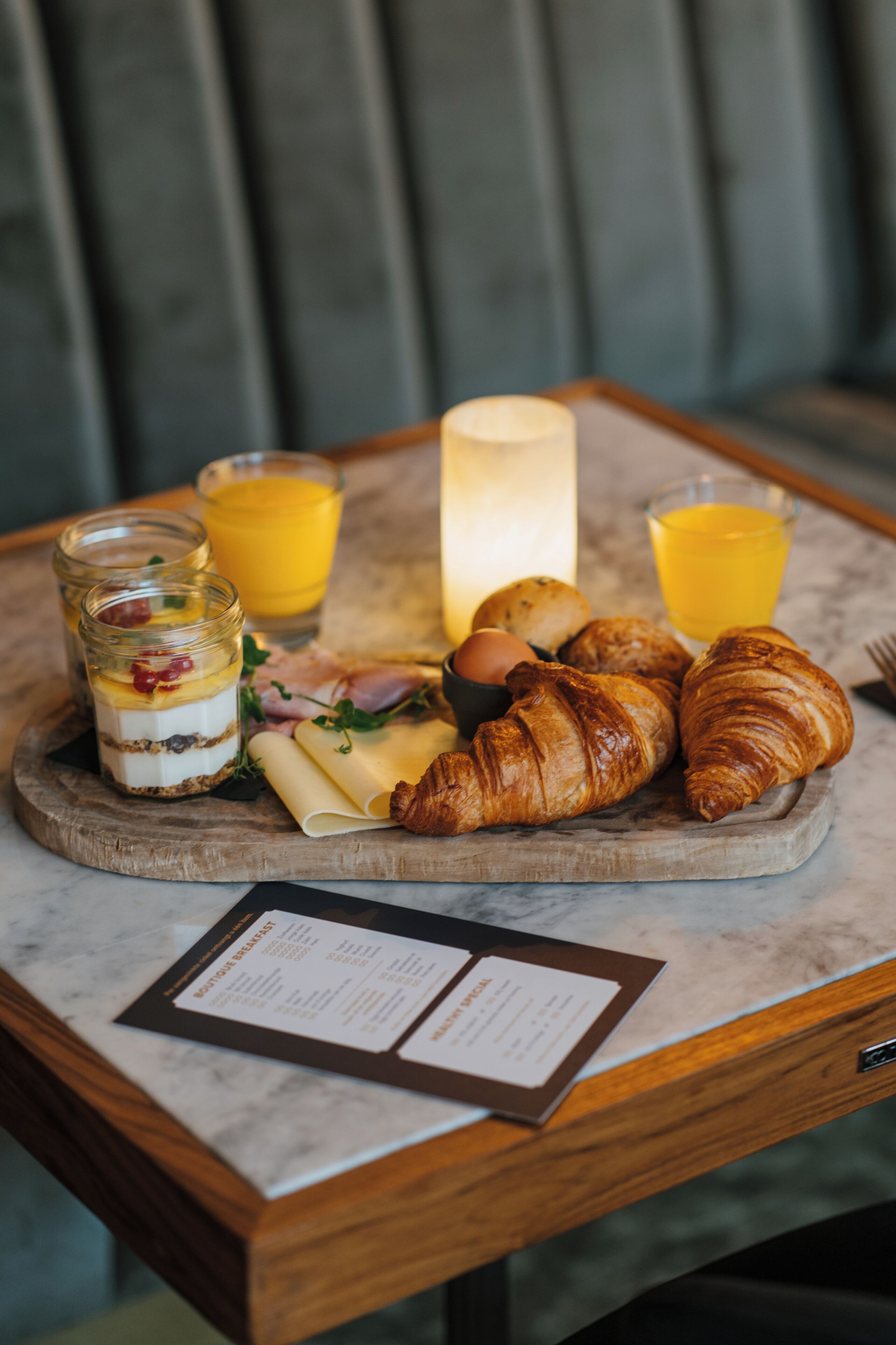 Ein Frühstücksbrett mit Croissants, Käse, Schinken und einem Obstparfait auf einer Marmortafel.