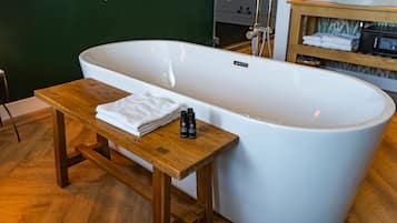 Un baño moderno con una bañera independiente, un banco de madera y una toalla.