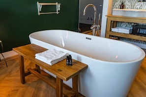 A modern bathroom with a freestanding bathtub, a wooden bench, and a towel.