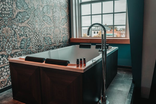 A modern bathroom with a freestanding bathtub, a window with a view of buildings, and a patterned wall.