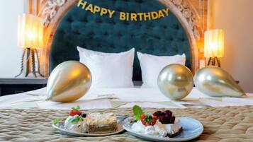 Una cama con un cabecero que dice 'Feliz Cumpleaños', dos mesitas de noche con lámparas y dos platos de postre sobre la cama.