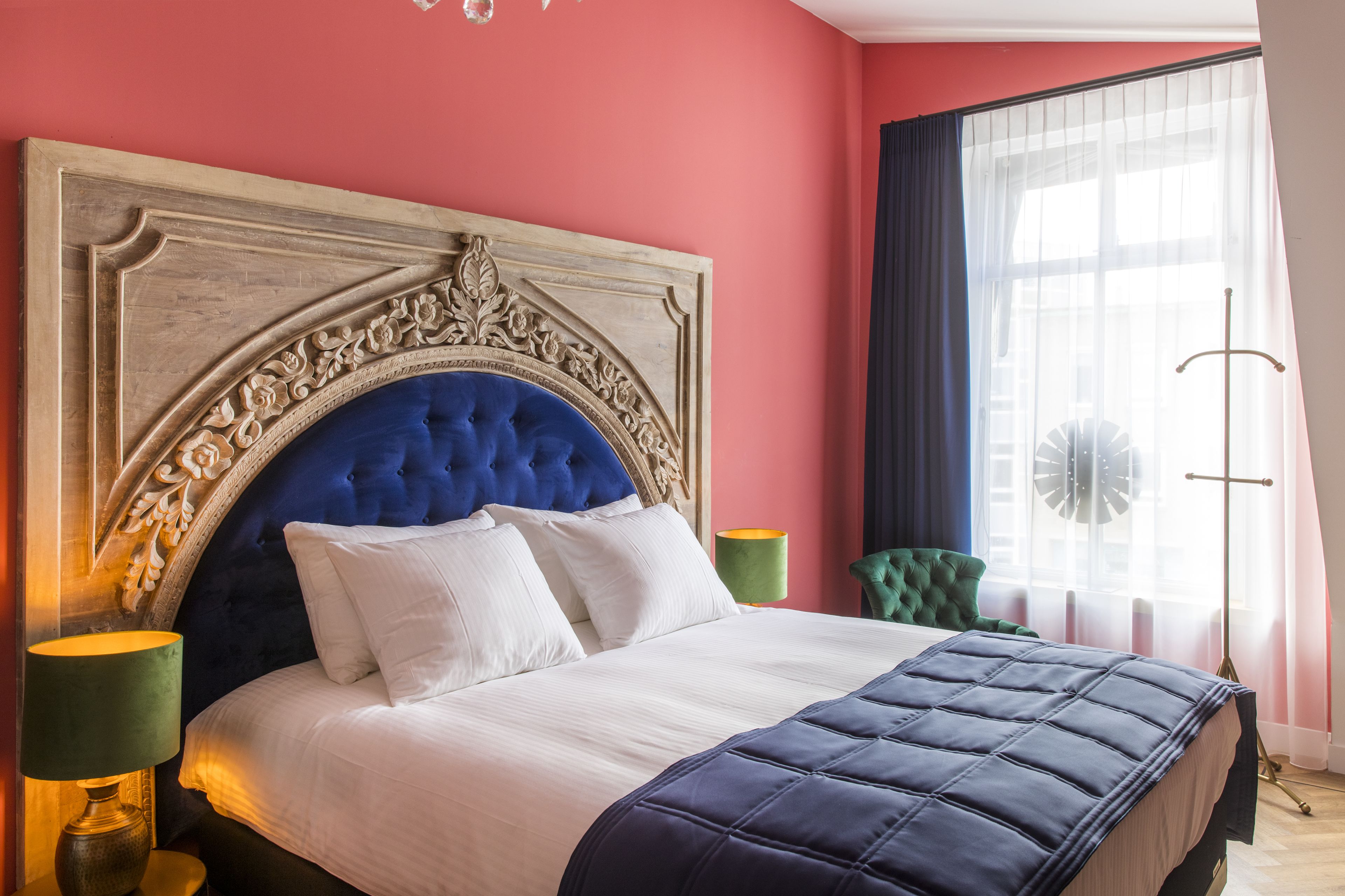 A bedroom with a large bed, a decorative headboard, a green chair, and a floor lamp.