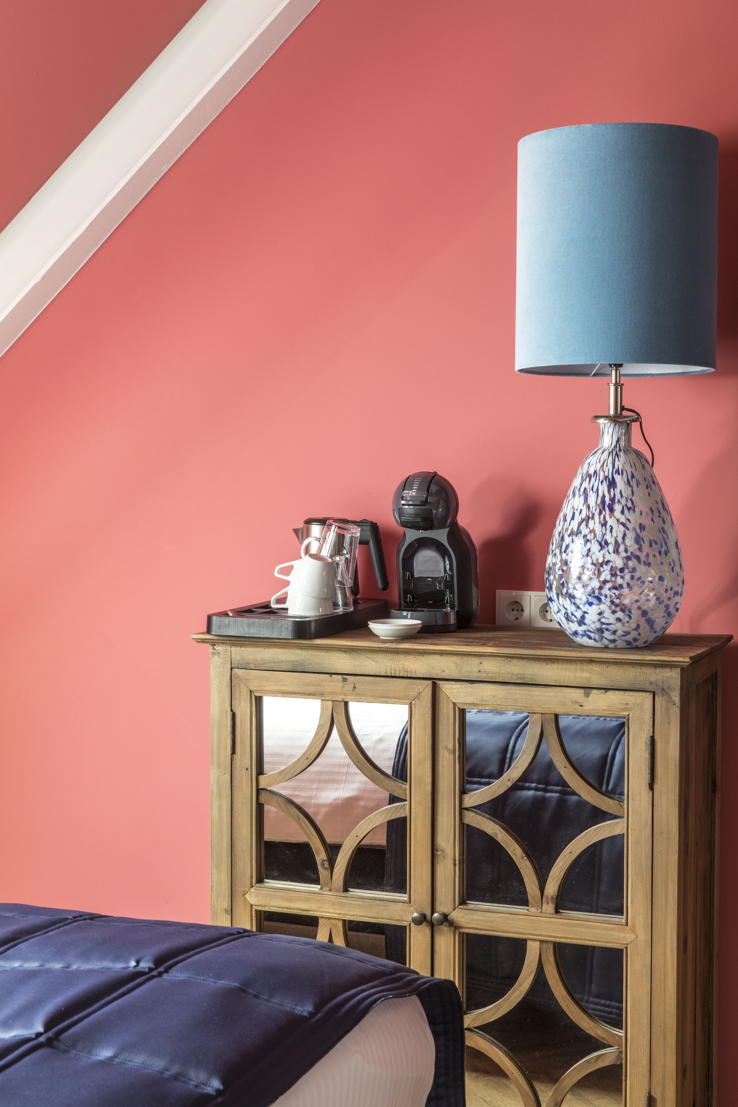 A wooden cabinet with a coffee maker, a lamp, and a vase on top.