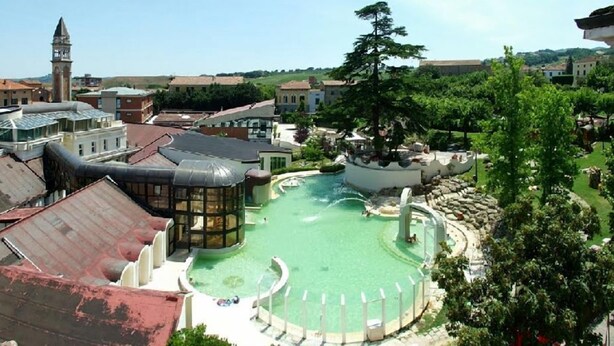 Una piscina con un design circolare, circondata da edifici e una torre sullo sfondo.
