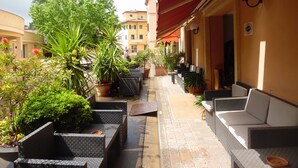Un corridoio esterno stretto con piante in vaso, posti a sedere all'aperto e un tenda rossa.