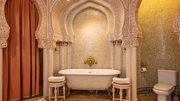 Un baño lujoso con un arco ornamentado, una bañera independiente y un inodoro.