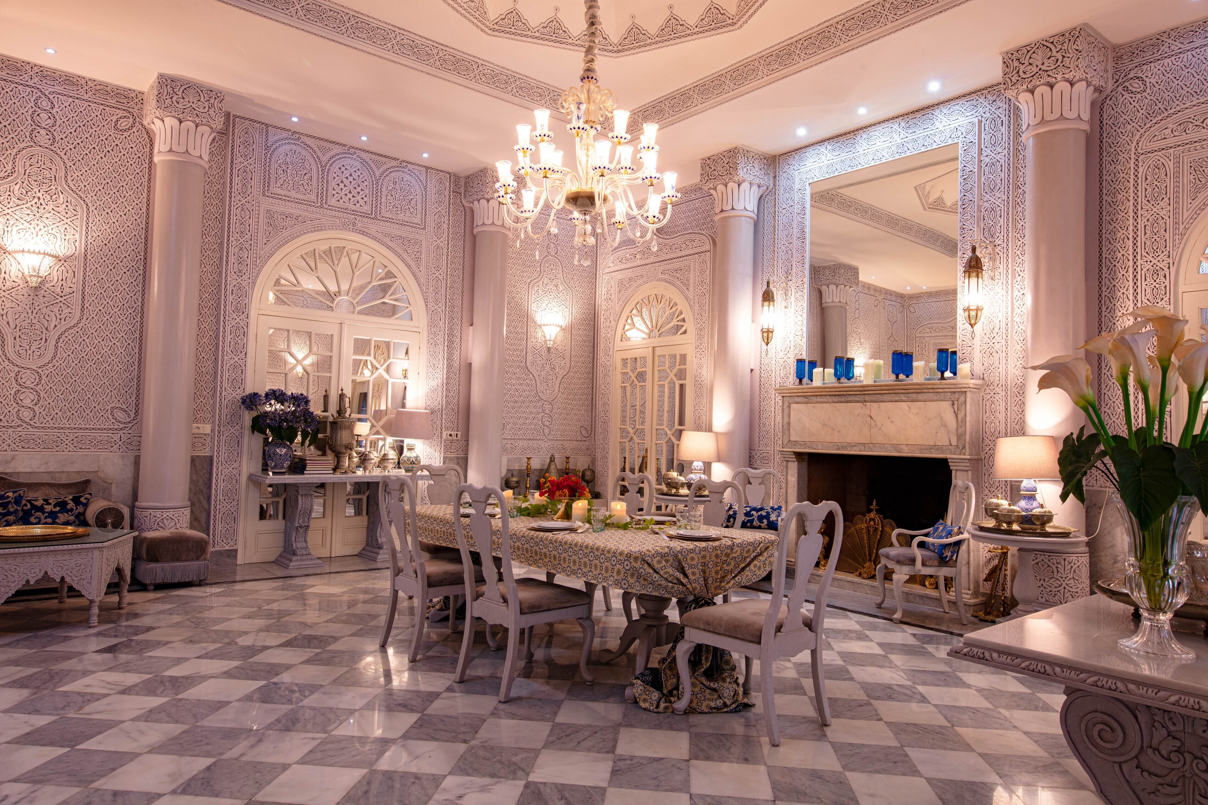 An opulent dining room with a checkered floor, ornate wall decorations, and a chandelier.