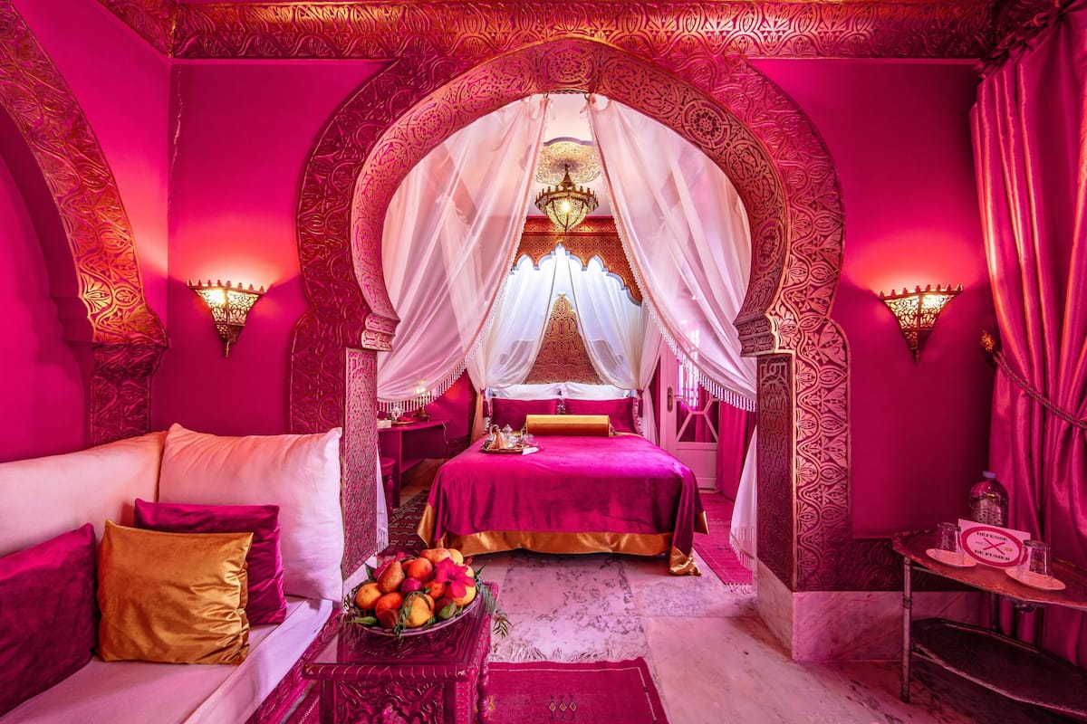 A room with a bed, a sofa, a chandelier, and a decorative archway.