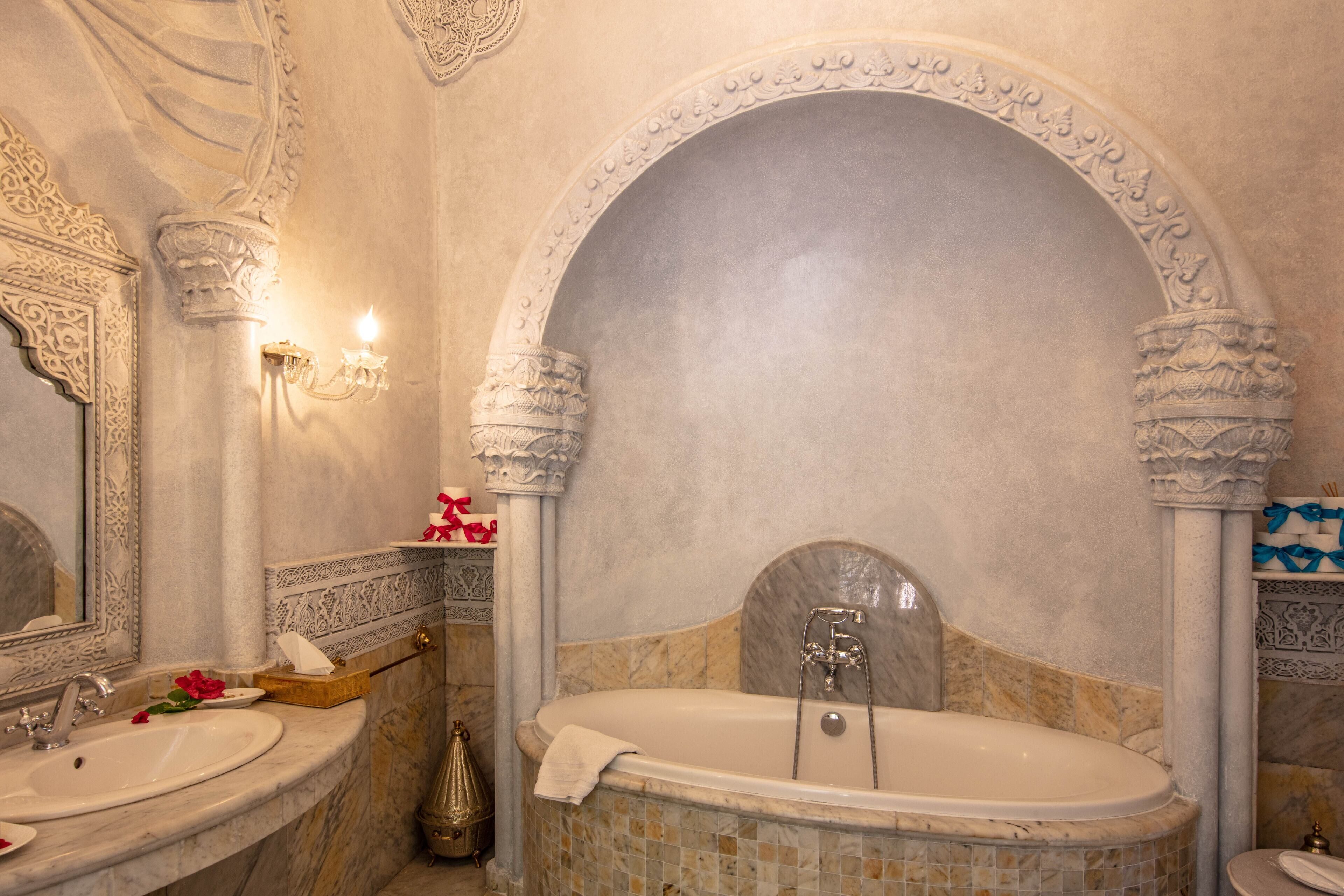 Un baño lujoso con una bañera grande, columnas ornamentales y un lavamanos de mármol.