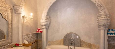 Un baño lujoso con una bañera grande, columnas ornamentales y un lavamanos de mármol.