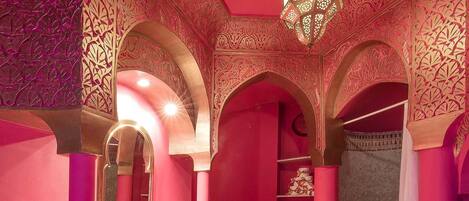 Un baño con decoración rosa, un espejo grande, un lavamanos y una zona de ducha.
