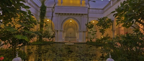 A courtyard with a fountain surrounded by ornate arches and a pool of water.