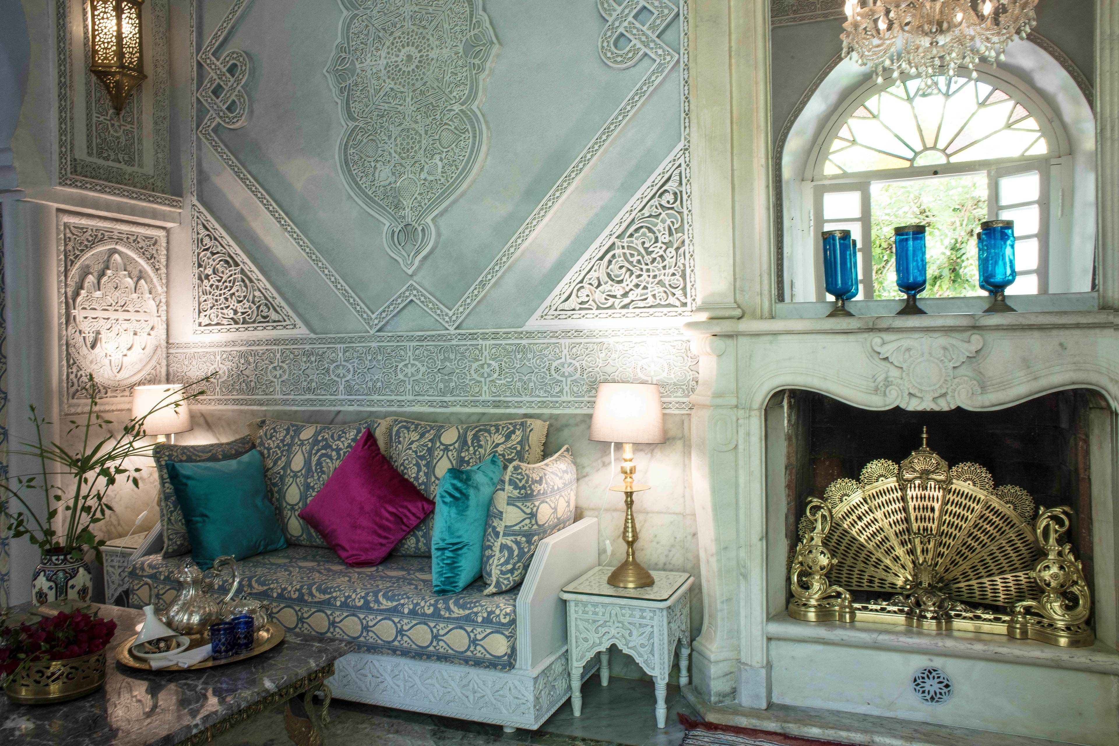 A room with a patterned sofa, a small table with a lamp, and a decorative fireplace.